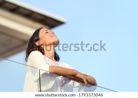 Relaxed adult woman breathing fresh air standing on a hotel balcony at summer