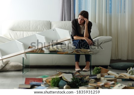 Sad tenant complaining after home robbery sitting on a couch in the night with messy living room Foto stock © 