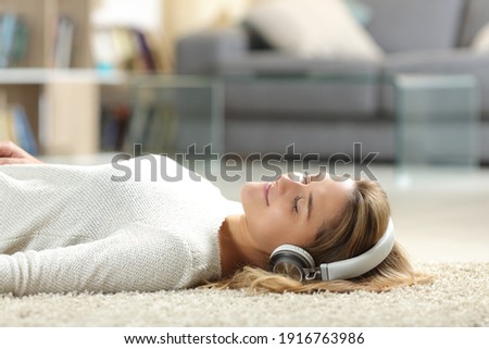 Relaxed woman listening to music with headphones lying on the floor at home