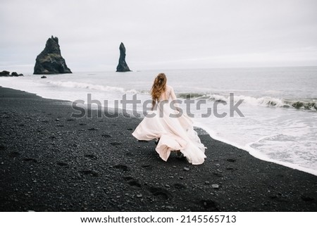 Girl in old old-styled wedding dress are running on the Black Sand beach in Vic, Iceland with rock islands on background. Сток-фото © 