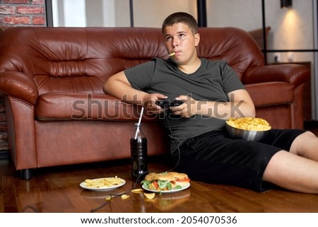 caucasian child boy eating fries. Fast food. Kid and unhealthy lifestyle concept. teenager boy playing console, have rest alone, sitting on floor, eating junk food, hamburgers and crisps on plate Сток-фото © 