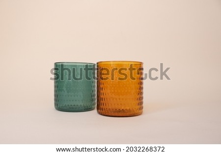 Glass orange and green cups on pink background with decoration. Emerald green cup. Amber orange cup. Couple glass cups with flowers. Tea cups. Coffee cups. Smoothies cup. Water cup.