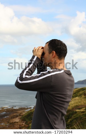 Adult man watching the sea or birds with binoculars