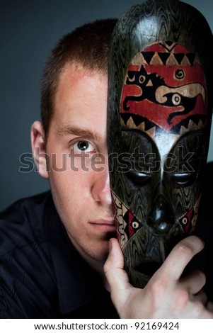 A man hiding behind a wooden antique mask (Sketch - hide suspense, mystery) on a dark background studio
