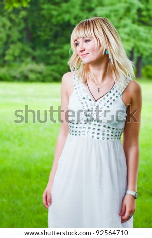 Portrait of a smiling white girl in white dress against the background of the summer foliage
