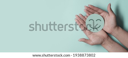 Hand holding green paper cut smile face on green background, positive thinking, mental health assessment , world mental health day concept