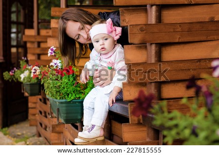 Beautiful young mother hugging little girl, looking over a wooden fence with flower beds