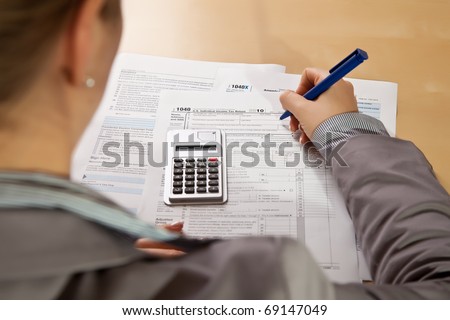 Woman hand filling income tax forms with calculator
