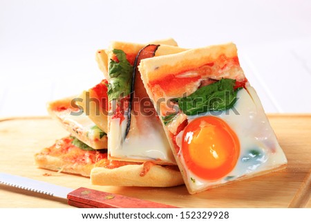 Cut rectangular pizza with egg Benedict and ham on a kitchen board