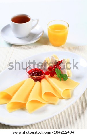 Two kinds of cheese on plate, cup of tea and glass of orange juice