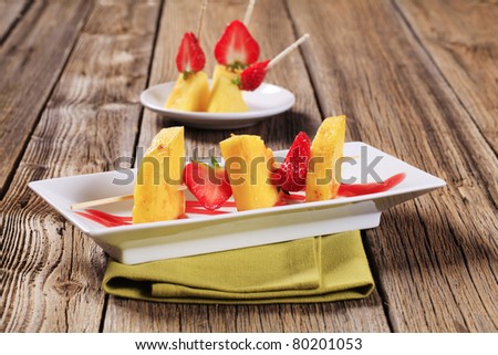 Pineapple and strawberry skewers garnished with sweet sauce