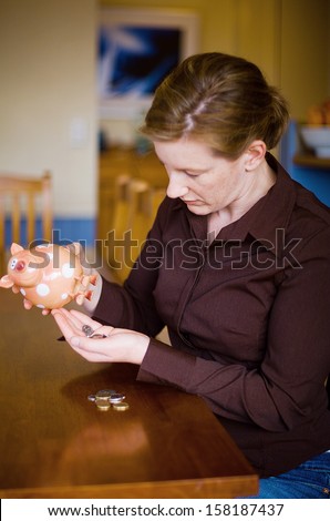 Adult female emptying money out of Toy money box, sitting at Kitchen table