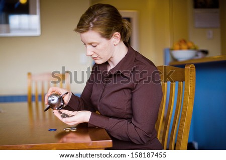 Adult female emptying money out of Toy money box, sitting at Kitchen table