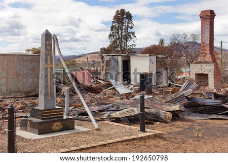 Ruins of a community hall destroyed by bushfire with War Memorial in foreground