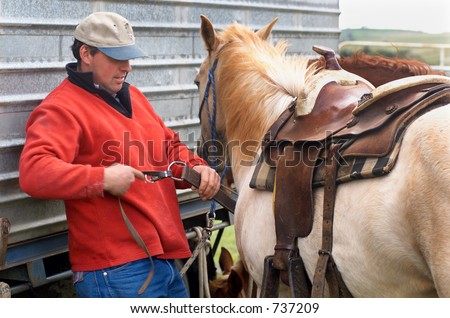 Cowboy fitting Western saddle to horse at Rodeo