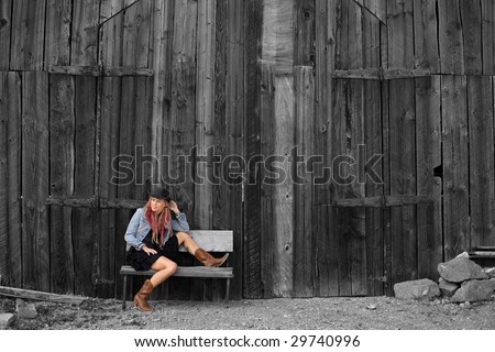 Young woman in Cowgirl style clothing sitting outside an old timber barn