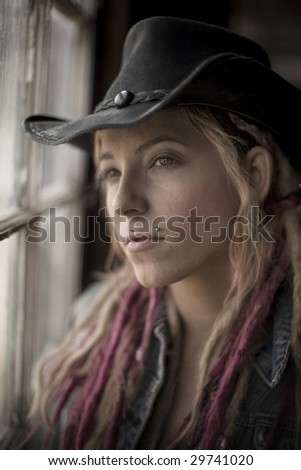 Portrait of young woman wearing leather hat looking out old barn window