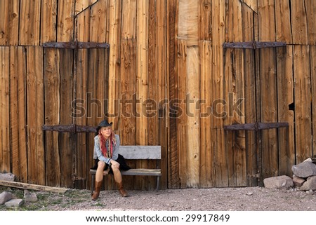 Young woman in Cowgirl style clothing sitting outside an old timber barn