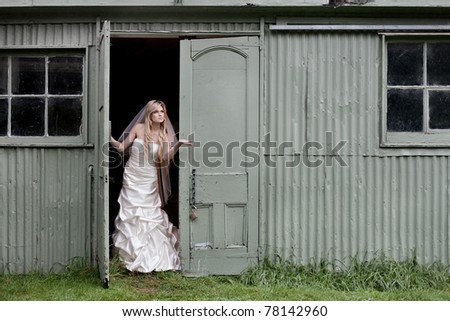 Beautiful young bride in her wedding dress, stands in doorway and checks for rain