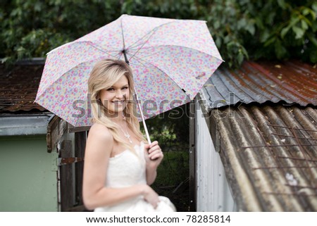 Beautiful young bride in her wedding dress, stands in the rain with colorful Umbrella