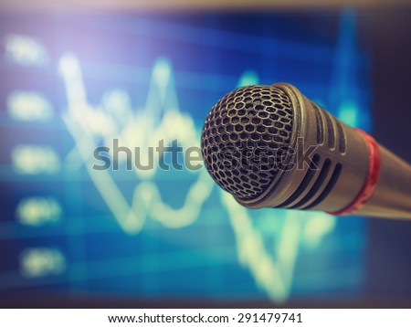 Vintage style photo of the microphone in hall or conference room with de focused financial trends background. Concept for Business Conference.