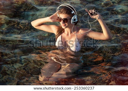 Young woman in headphones listening music and enjoying beautiful sunset in the sea. Top view