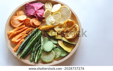 Vegetable chips, crispy vegetable snacks, veggie chips, mixed vegetable chip dehydrated snack on wooden plate isolated on white background. Healthy food concept.