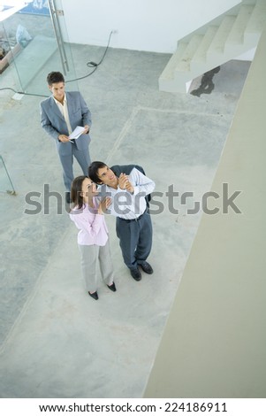 Real estate agent showing unfinished house to enthusiastic young couple, high angle view