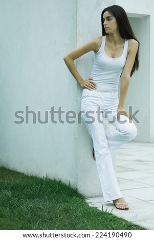 Woman standing, leaning against wall, hand on hip, looking away, full length