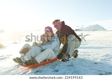 Mature man crouching behind sled with two daughters, smiling at camera