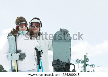 Young couple dressed in ski wear, man holding snowboard, woman holding ski sticks
