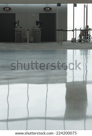 Reflection on airport floor, person in wheelchair waiting for assistance in background