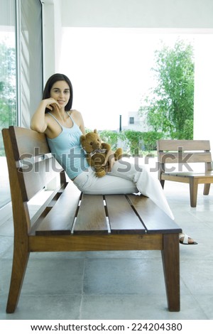 Woman sitting on patio furniture holding teddy bear, full length