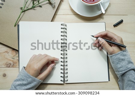 close up female hands writing on an opened notebook on wooden table. Top view. Writing concept