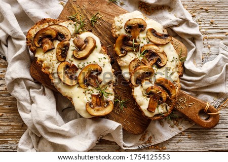 Toasted sandwich from traditional sourdough bread with cheese and brown mushrooms seasoned with rosemary herb on a wooden board, top view