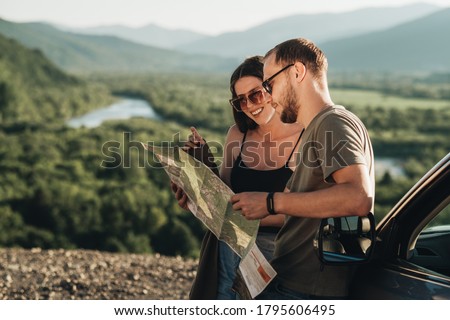 Travelers Couple on Road Trip, Man and Woman Using Map on Journey Near Their Car Over Beautiful Landscape