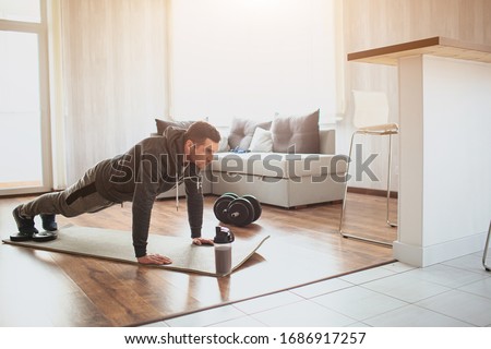 Young ordinary man go in for sport at home. Full size picture of regular ordinary guy stand in plank position alone in room. Beginner try to do his best and exercise. Hardworking real person