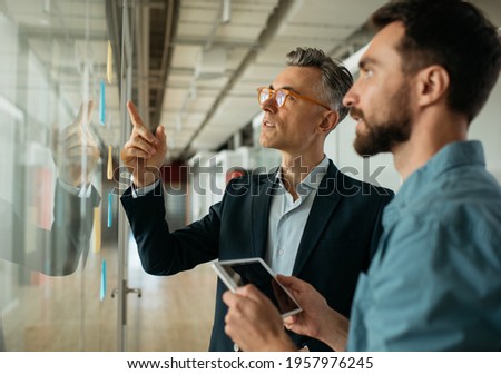 Business people meeting planning start up, talking, discussing ideas, brainstorming. Scrum master using sticky notes standing near planning board in modern office. Agile methodology, scrum concept	 Foto stock © 
