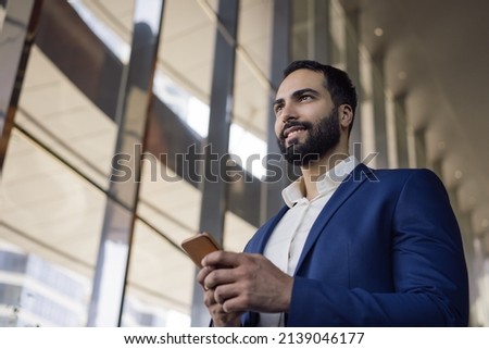 Handsome smiling middle eastern business man using mobile phone working in modern office. Confident arabian manager wearing formal wear text messaging looking at window. Successful business  ストックフォト © 