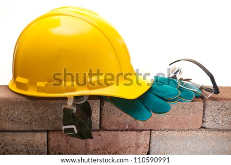 Safety helmet, work gloves and safety glasses on the brick wall on a white background