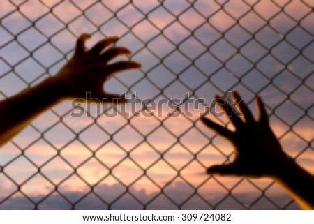 blury hand put on the metallic fence at the sunset