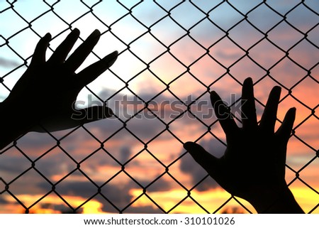 hand put on the chain link fence on an evening sunset with depth of field, out of focus sunset. Sunset with amazing sunset background. Industrial sunset.Silhouette on sunset sky