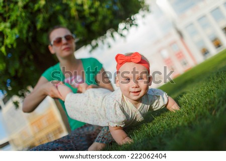 Mom doing yoga with your child. Baby crawling on the grass on a background of sitting his mom. The kid runs away from his mother.