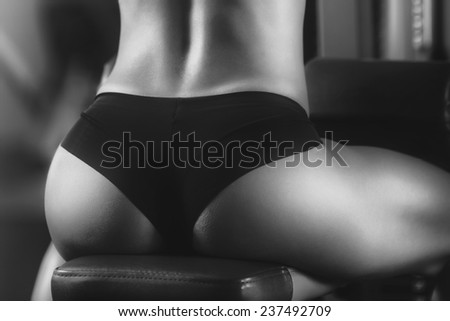 Black and white photo of a strong woman from behind. Sexy fitness girl in sport wear with perfect body in the gym posing before training set. Attractive fitness woman, trained female body
