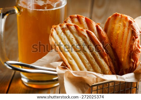 Toasted slices of bread with a golden crust neatly stacked in a metal stand on a wooden brown background and a glass of beer