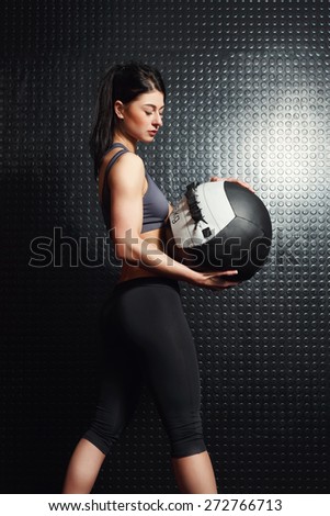 Attractive, muscular young woman holding medicine balls for fitness against the black wall