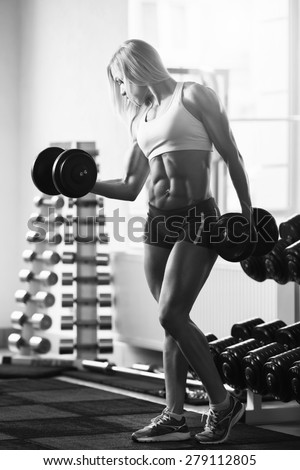 Black and white photo of a strong woman. Strong woman bodybuilder with white hair and tanned body pumps up the muscles lifting dumbbells in the gym. Vertical frame with space for text