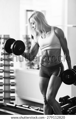 Black and white photo of a strong woman. Strong woman bodybuilder with white hair and tanned body pumps up the muscles lifting dumbbells in the gym. Vertical frame with space for text