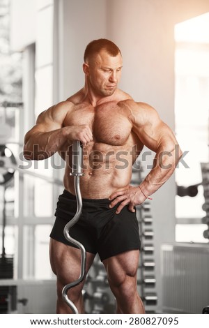 Strong man in black shorts holding a curved barbell in the gym and looks aside