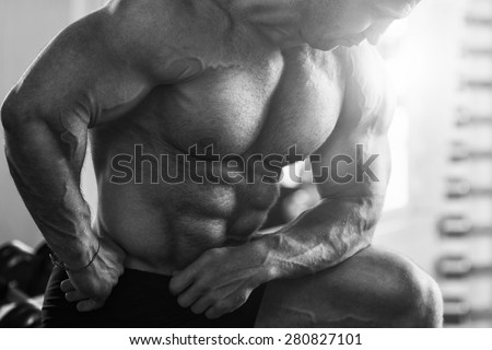 Black and white photo. Brutal man bodybuilder shows muscles of the chest, abdomen and arms. Strong man flexing his muscles. Part of the body close-up
